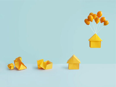 Paper house floating from being tied to balloons with other house behind. image number null